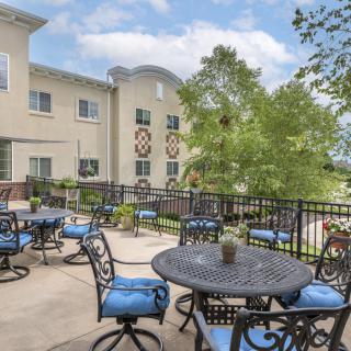 A sunny outdoor patio with tables and chairs, adjacent to a building.