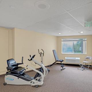 A small fitness room with exercise equipment, including a recumbent bike and other workout machines, illuminated by natural light from the window.