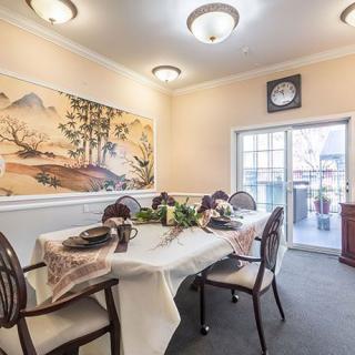 An elegant dining room featuring a well-set table, ornate chairs, a decorative painting, and ambient lighting.