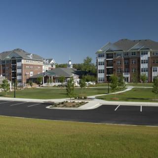 A view of modern apartment buildings with a landscaped area and parking lot.