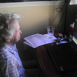 An elderly person sitting at a desk, using a computer.