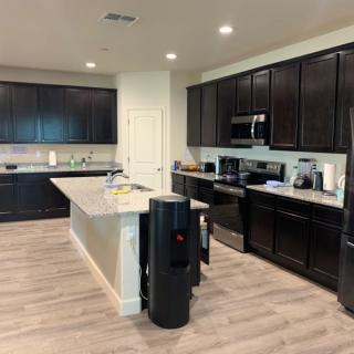 A modern kitchen with dark cabinets, featuring a spacious island and wood flooring.