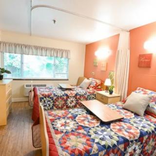 A cozy bedroom with twin beds covered in colorful quilted bedspreads, featuring warm lighting and a window view.