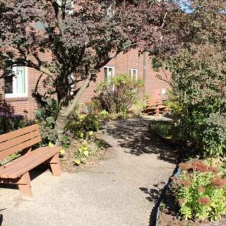 A peaceful garden area with benches and a pathway surrounded by trees and shrubs.