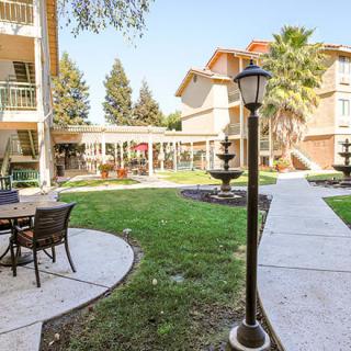 A serene courtyard at an apartment complex, featuring outdoor seating, a fountain, and well-maintained landscaping.