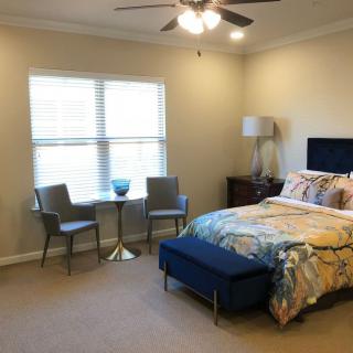 A cozy bedroom featuring a bed with colorful bedding, two chairs with a small table by the window, and a lamp in the corner.