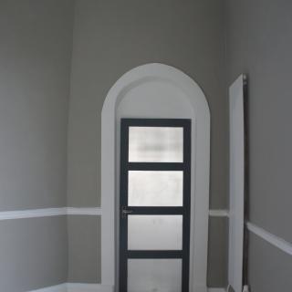 A minimalist interior with an arched door featuring frosted glass panels set against gray walls.