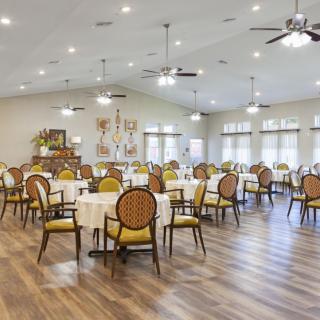 A spacious dining area with elegant tables and chairs, featuring ceiling fans and large windows.