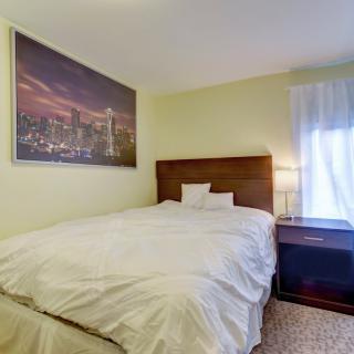 A cozy bedroom with a neatly made bed, nightstand, and a large cityscape painting on the wall.