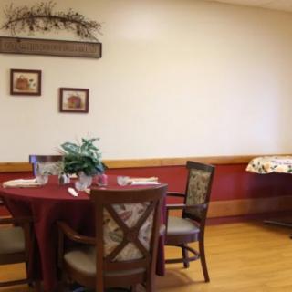 A cozy dining area with a table set for guests, featuring elegant chairs and simple wall decorations.