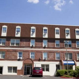 A multi-story brick building with several windows and a central entrance, accompanied by a parked car in front under a clear blue sky.