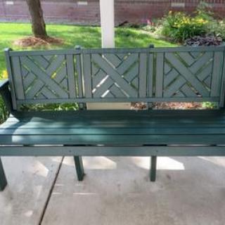 A green outdoor bench with a decorative backrest on a porch.