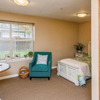 A cozy bedroom interior with a teal armchair and white bed near a window.