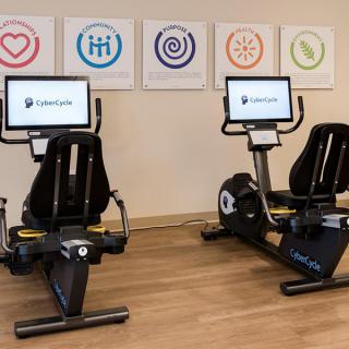Two stationary exercise bikes in a gym setting with digital displays.