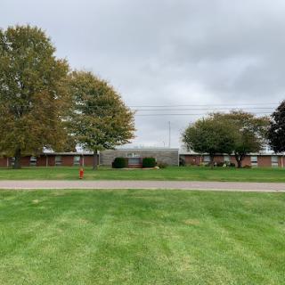 A view of a building surrounded by trees and green grass under a cloudy sky.