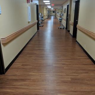 A view of a hospital corridor featuring wooden flooring and soft lighting.