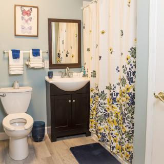 A modern bathroom with a floral shower curtain, wall mirror, and neatly arranged towels.