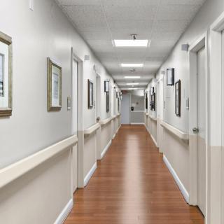 A clean, well-lit hospital corridor with wooden flooring and framed artwork on the walls.