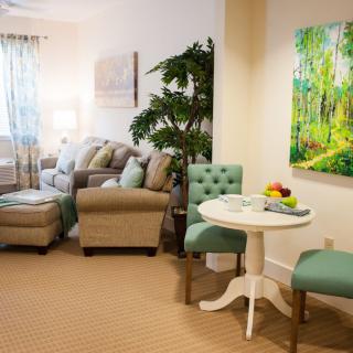 A cozy and well-decorated living room with a sofa set, armchair, a small round table with chairs, and vibrant wall art.