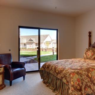 A cozy bedroom with a large bed, armchair, and natural light streaming through a sliding glass door.