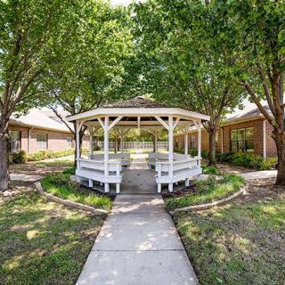 A charming white gazebo surrounded by trees and greenery, with a pathway leading to it.