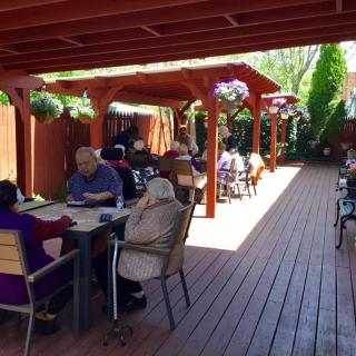 A group of people sitting and socializing on a sunny outdoor patio with wooden decking.