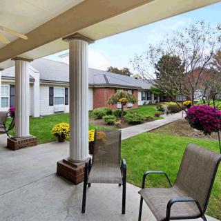 A peaceful outdoor patio area with chairs, surrounded by a well-maintained garden with flowers and columns.