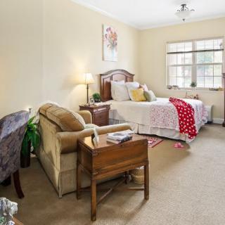 A cozy bedroom with a bed, armchair, and wooden furniture under soft lighting.