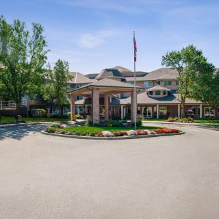 A well-maintained building entrance with surrounding trees and a flagpole at the center of the driveway.