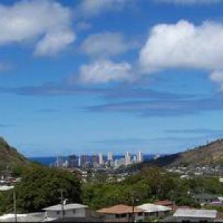 A scenic view of the city skyline nestled between two mountains with an ocean in the distance and fluffy clouds in the sky.