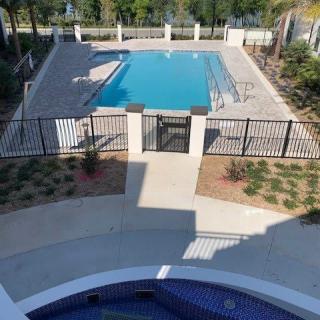 A fenced outdoor swimming pool area with surrounding landscaping on a sunny day.