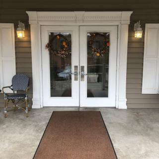 A welcoming porch with double doors adorned by wreaths and a cozy chair.
