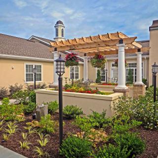 A beautifully landscaped garden with a pergola and flowering plants in front of a building.