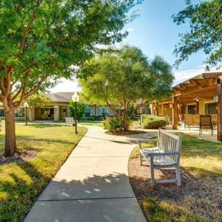 A peaceful outdoor scene with a walkway, trees, and benches under the clear sky.