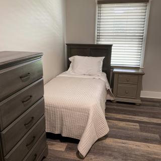 A simple bedroom with a single bed, dresser, and nightstand.