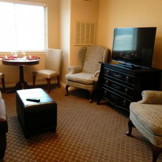 A cozy living room with a TV, chairs, a small table, and a window.