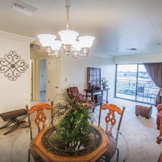 A cozy living and dining area featuring a round table with ornamental chairs, a chandelier, and a view through large windows.
