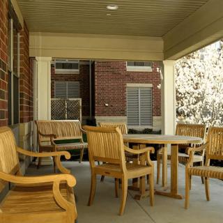 A cozy outdoor porch with wooden chairs and a table, set against a brick building.
