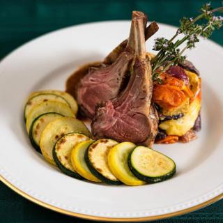 A gourmet plate featuring lamb chops with grilled zucchini and garnished vegetables.