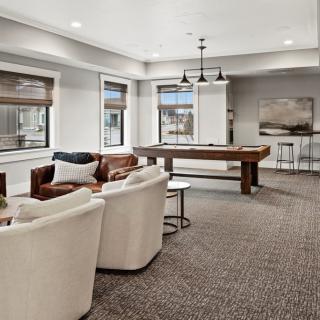 A modern game room featuring a pool table, comfortable seating, and large windows providing ample natural light.