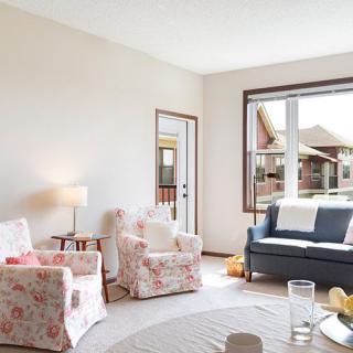A cozy living room featuring floral armchairs, a dark blue sofa, and a large window letting in natural light.