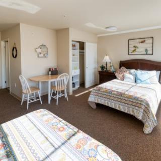 A cozy hotel room with two double beds, a small dining table, and simple decor.