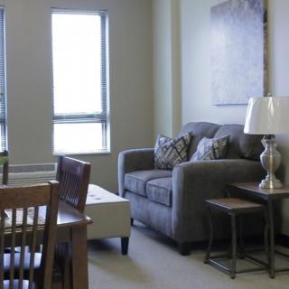 A cozy living room with a sofa, lamp, and tables near a window.