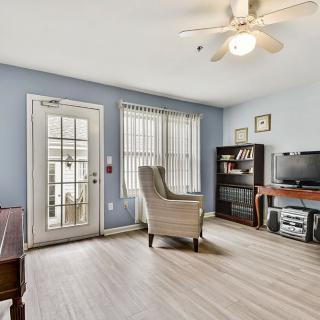 A cozy living room with blue walls, featuring an armchair, television, and bookshelf. The space is well-lit with natural light from large windows and a glass door.