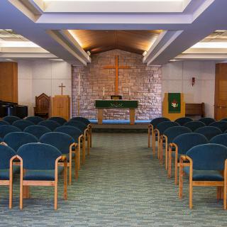 An empty chapel interior with rows of chairs facing the altar.
