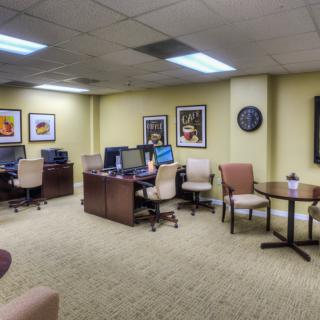 A spacious office area with multiple workstations, featuring computers on desks, comfortable chairs, and artwork on the walls.