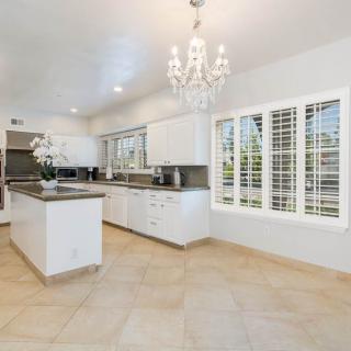 A modern kitchen with white cabinets, a central island, and a chandelier, featuring tiled floors and bright lighting.
