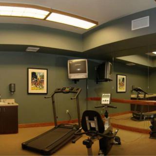 A small gym room equipped with a treadmill, stationary bike, and a wall-mounted television.