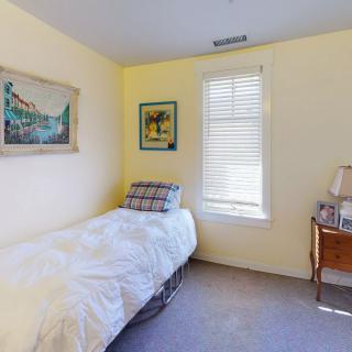 A minimalist bedroom with a single bed, artwork on the walls, and a window letting in natural light.