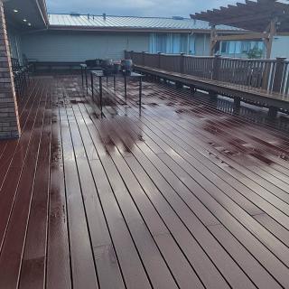 A spacious rooftop deck with wooden flooring and wet surfaces, featuring railings and benches.